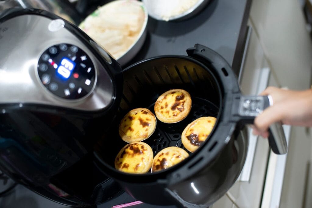 un air frayer ouvert avec un dessert à l'interieur des pastels de nata pour illustrer l'article air fryer comment ça marche