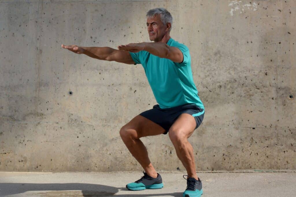 un homme âgé qui fait des squats dans le cadre du sport pour personne âgée à la maison